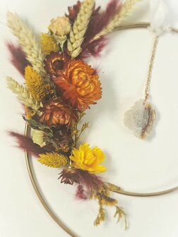 2 Gold rings with agate pendant surrounded by colorful dried flowers in orange, red and yellow tones.