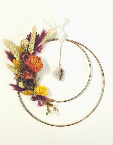 2 Gold rings with agate pendant surrounded by colorful dried flowers in orange, red and yellow tones.